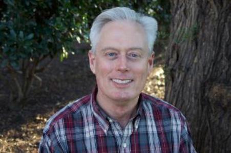 A man in a plaid shirt smiling outdoors.