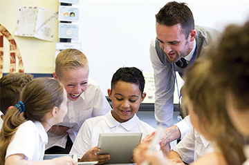 A teacher and students engaged with a tablet in a classroom.