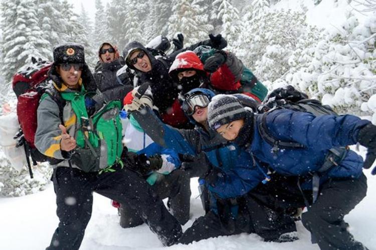 A group of students in winter gear pose in snowy forest.