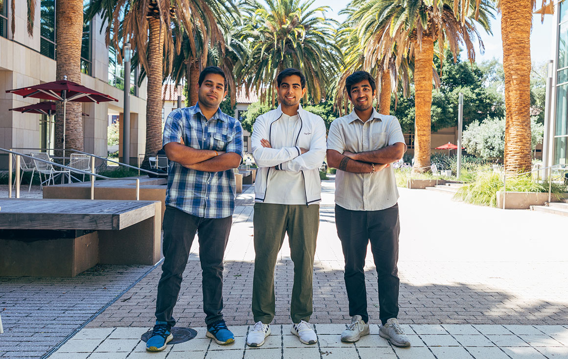 Three men pose in front of palm trees.