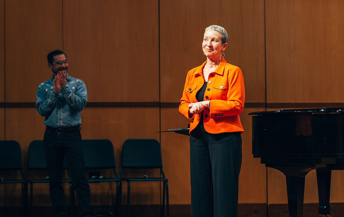 Woman stands centerstage as student applauds.