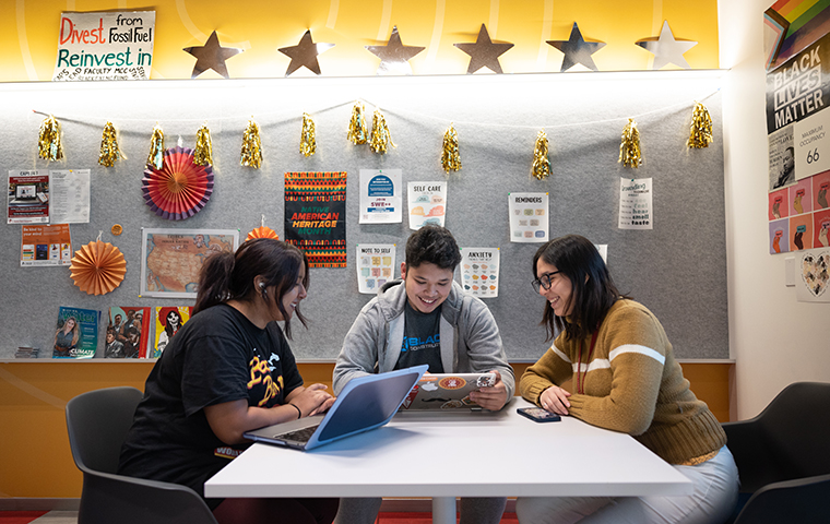 Three students studying at a table in front of a yellow wall in DISC