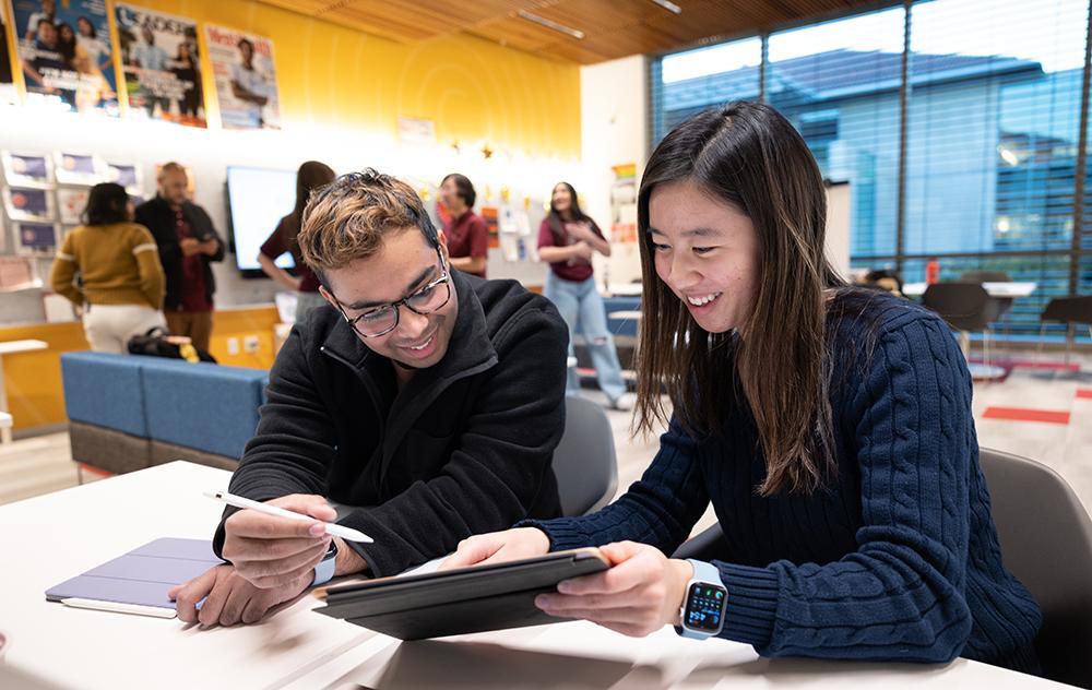 Two students look at a sheet of paper at a table in DISC in SCDI