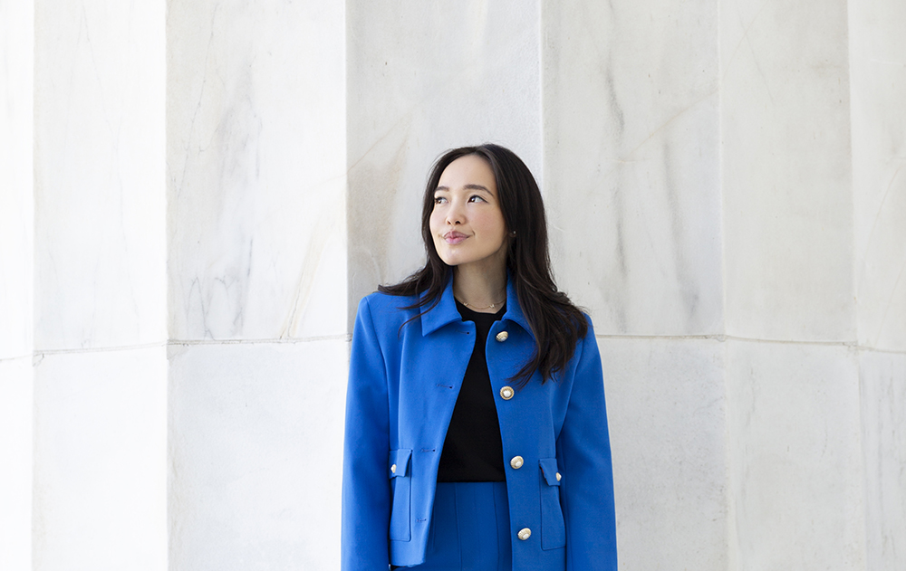 A woman in a blue outfit standing against a marble background.