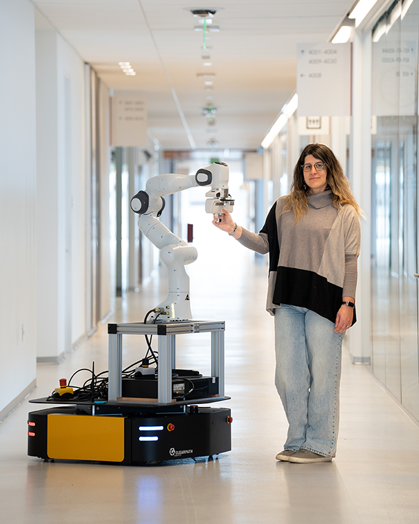 A woman stands in a white hallway with a large robotic arm on a mobile platform.