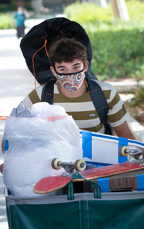 Student pushes dolly with skateboard in it at Move-In Day 2021