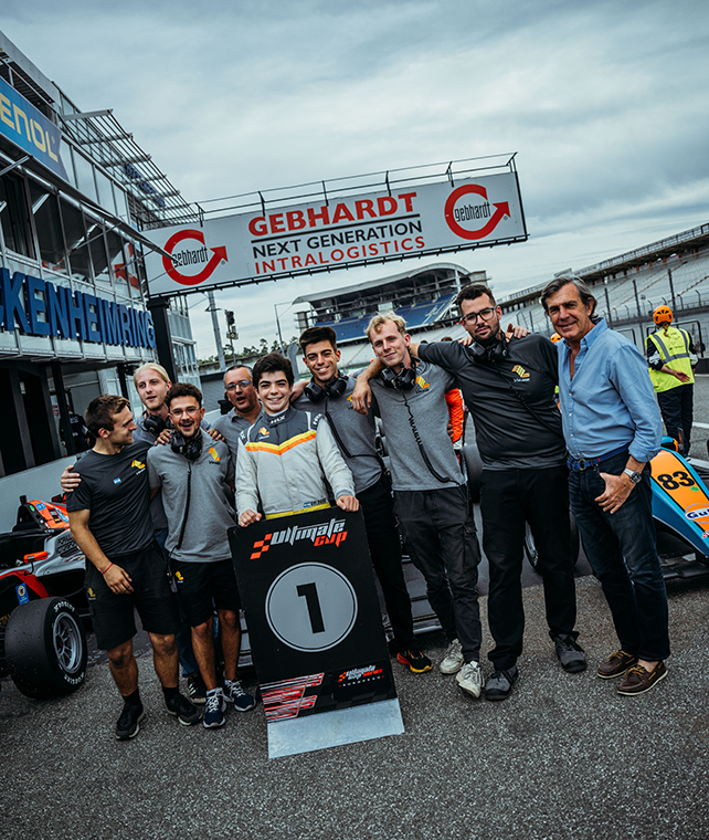 A young racecar driver celebrates by a 1st place trophy and his pit crew.