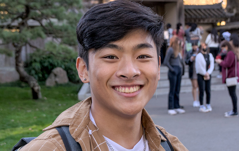 A person smiling outdoors with people in the background.