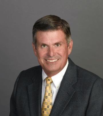 Man in suit smiling against a gray background.