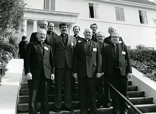 A black and white photo of a group of smiling priests outside the old JST building