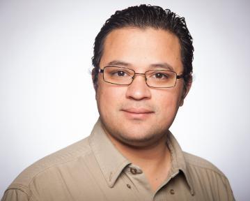 A person wearing glasses and a beige shirt against a plain background.