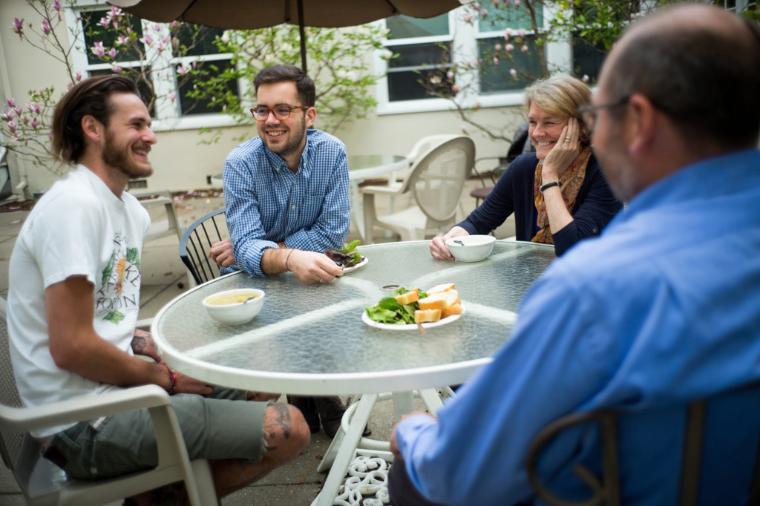 Alt text: Four people having a meal at a round outdoor table.