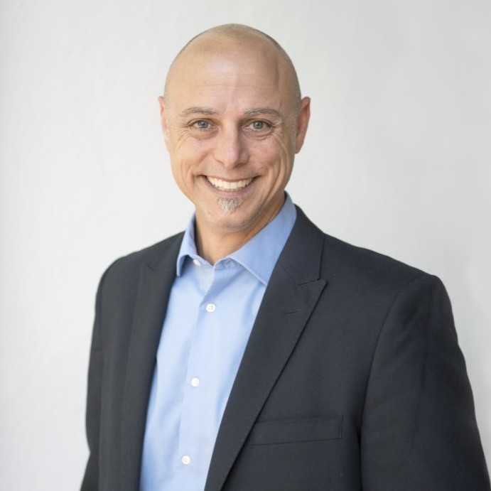 A man in a suit smiling against a plain background.