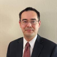 A person in a suit and tie standing against a plain background.