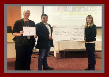 Three people standing in front of a whiteboard, one holding a large check.