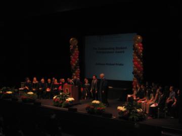 Large group on stage with lighting and a central screen displaying 