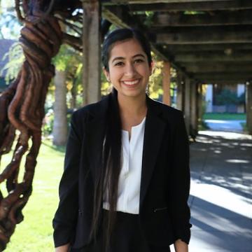 Young person smiling outdoors under a pergola.
