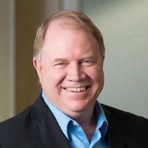 A person smiling in a suit and blue shirt.