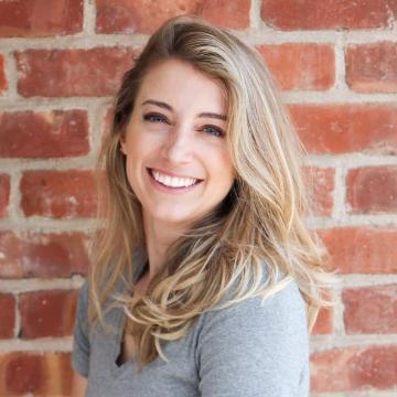 A woman smiling in front of a brick wall.