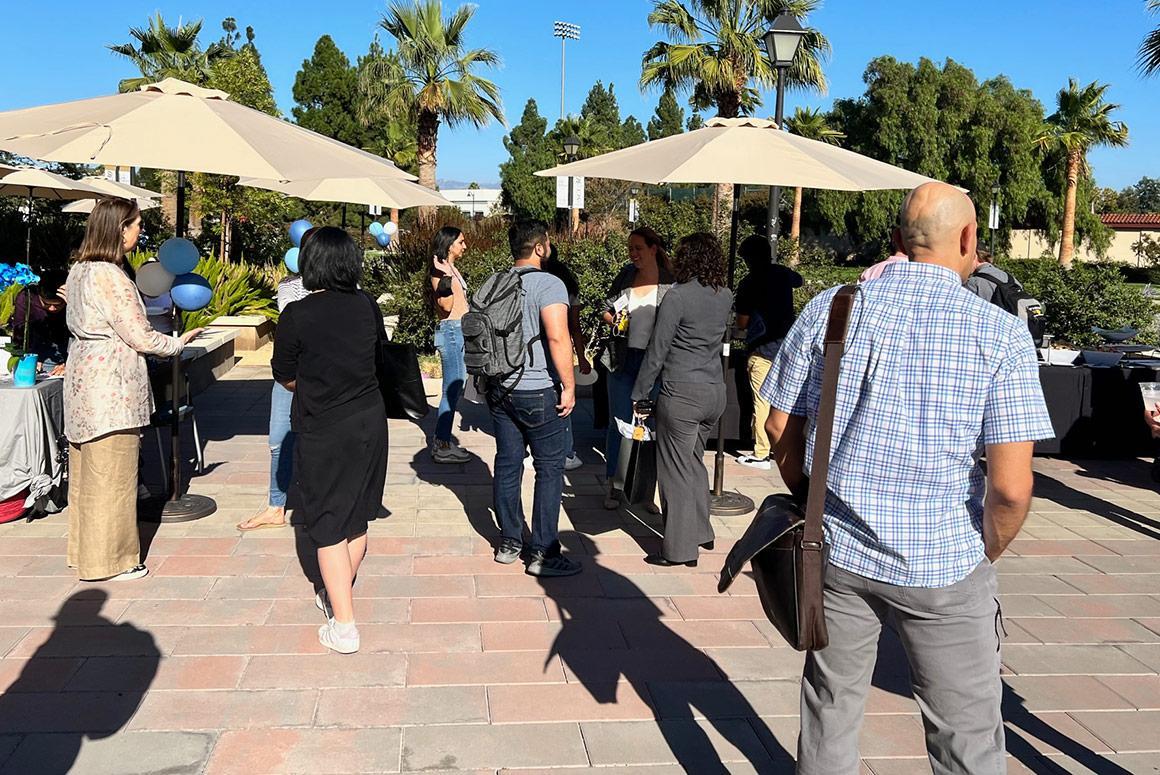 People socializing at 'Ciocca Center Beach Day' event with sun umbrellas in the background.