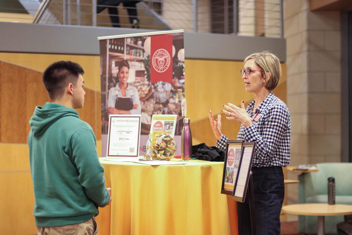A person speaking to another person at a booth with brochures.
