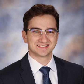 A person in a suit and tie smiling with a blurred background.