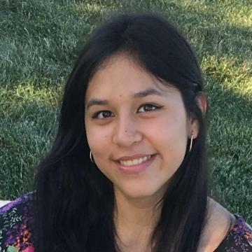 A person smiling outdoors with grass in the background.