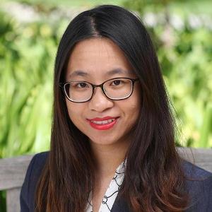 A person wearing glasses and a dark blazer, smiling at the camera.