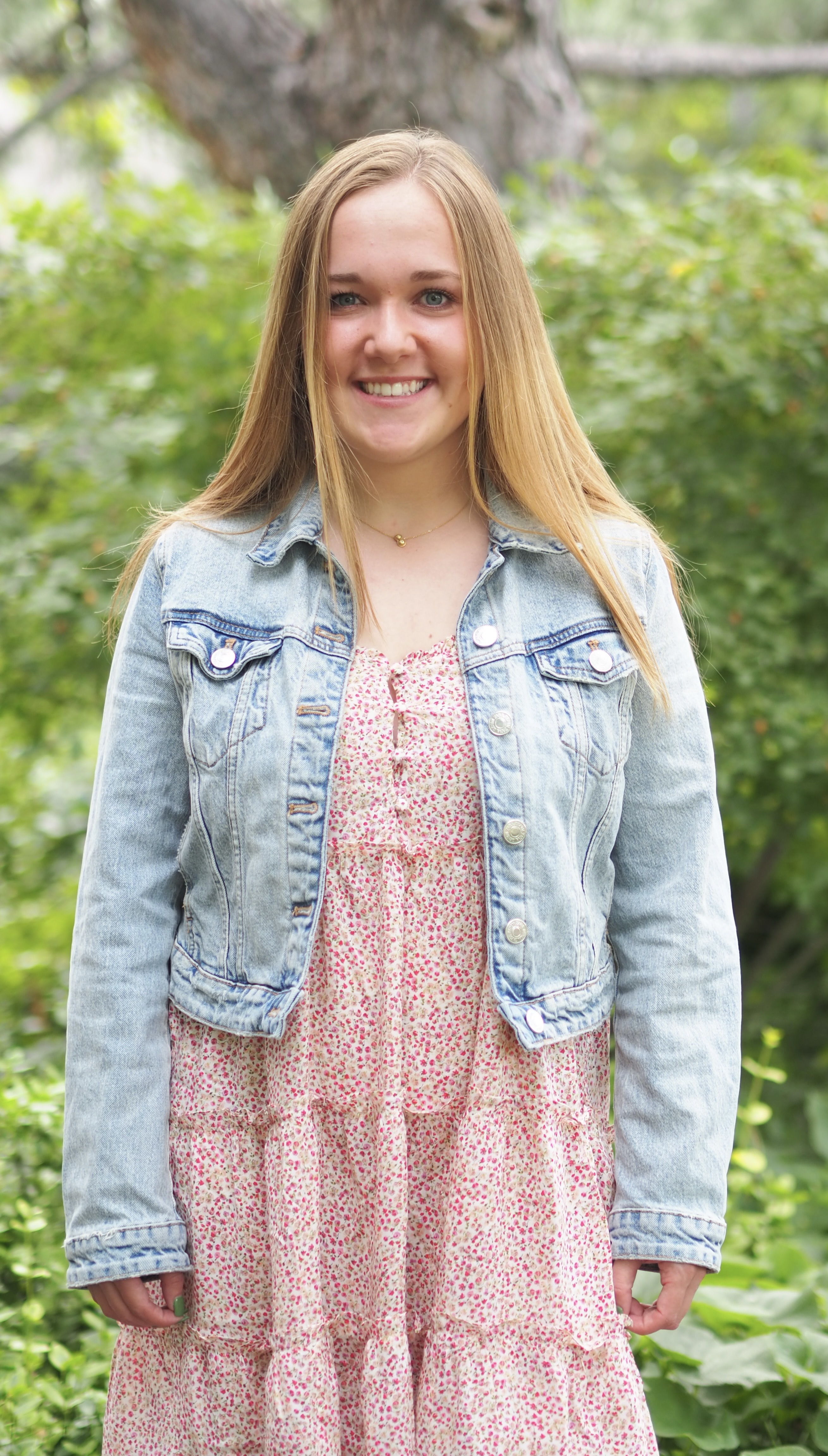 A person wearing a denim jacket over a pink floral dress outdoors.