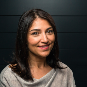 A woman smiles in front of a dark, blurred background.