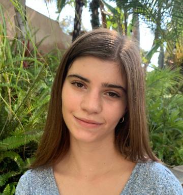 A person smiling, standing in front of green plants outdoors.