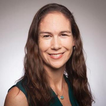 A woman smiling, wearing a dark top, with a plain background.