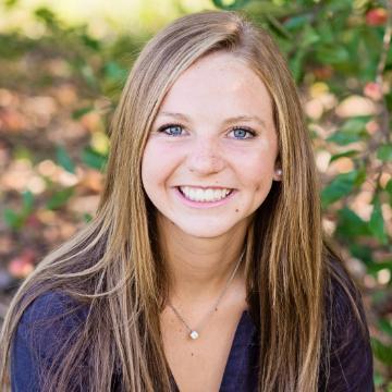 A person smiling in front of greenery.