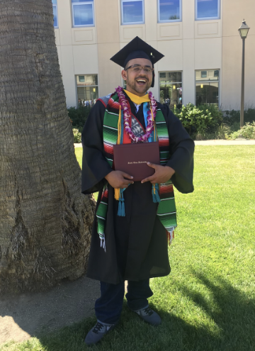 A person in graduation attire holding a diploma outdoors.