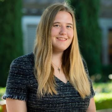 A person standing outdoors, smiling, in front of a building.