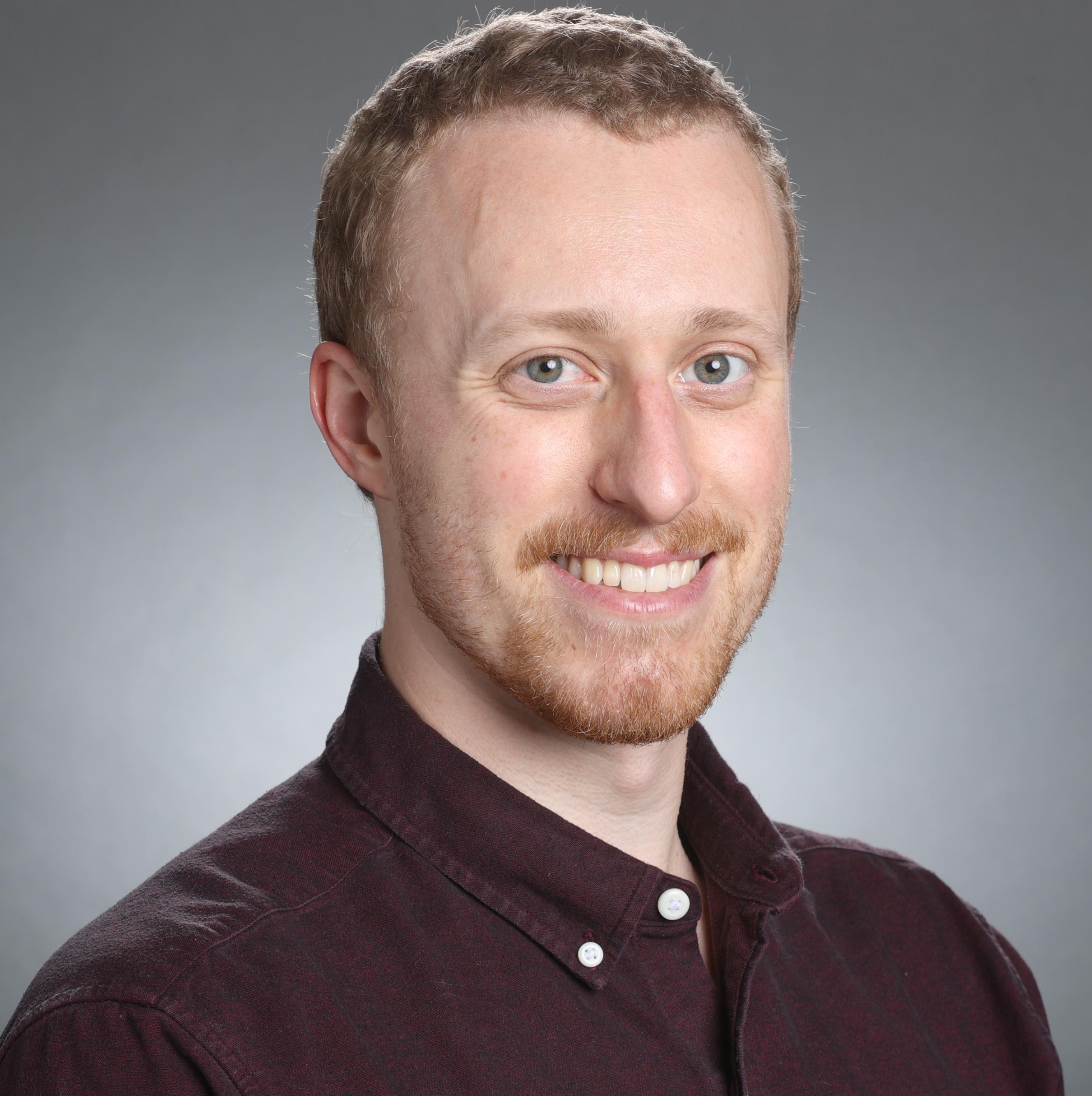 A person in a dark shirt poses against a gray background.