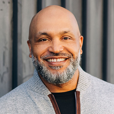 A smiling person in a light-colored jacket outdoors.