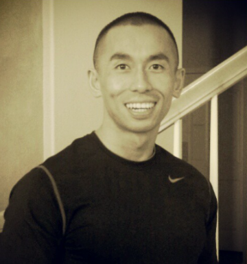 Smiling man standing indoors in front of stairs.