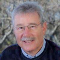 A smiling person seated with a nature background.