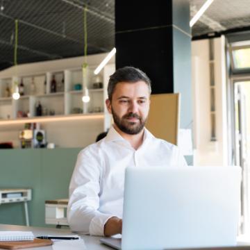 Young businessman working in his office, sitting at the desk, laptop and tablet in front of him