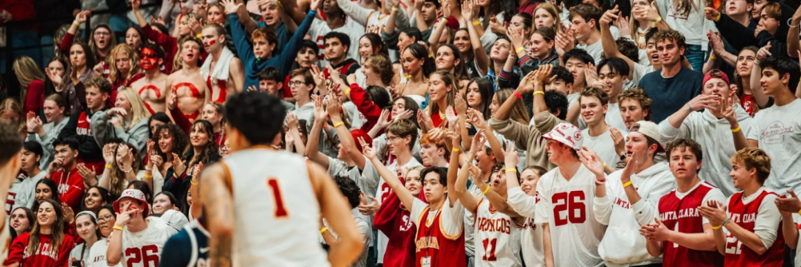 A Broncos player jogs by a large crowd of cheering students at a basketball game