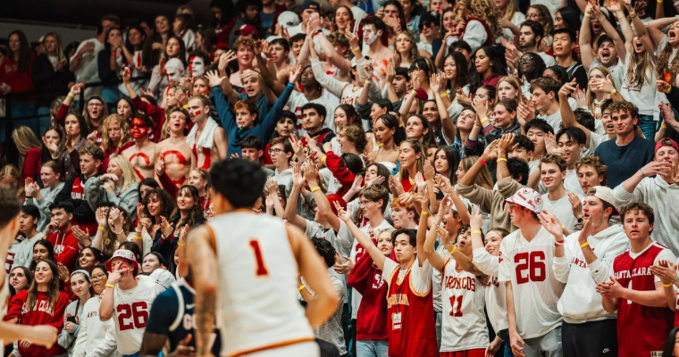 A Broncos player jogs by a large crowd of cheering students at a basketball game image link to article