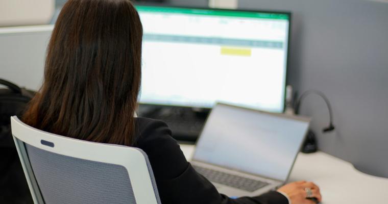 Businesswoman looking at spreadsheets on laptop and monitor