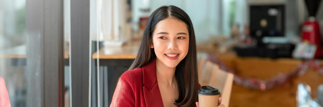 Happy smile young businesswoman in a red suit sitting holding coffee with laptop computer in café