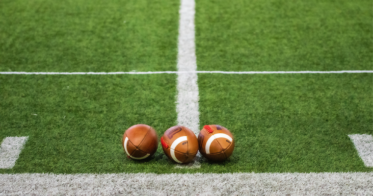 Three American footballs next to each other on a turf field