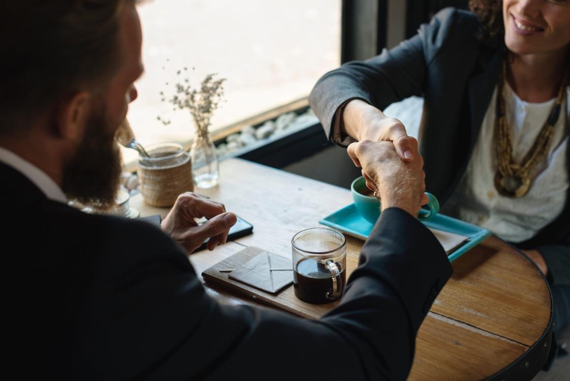 Two entrepreneurs in business attire shaking hands across a table at a restaurant