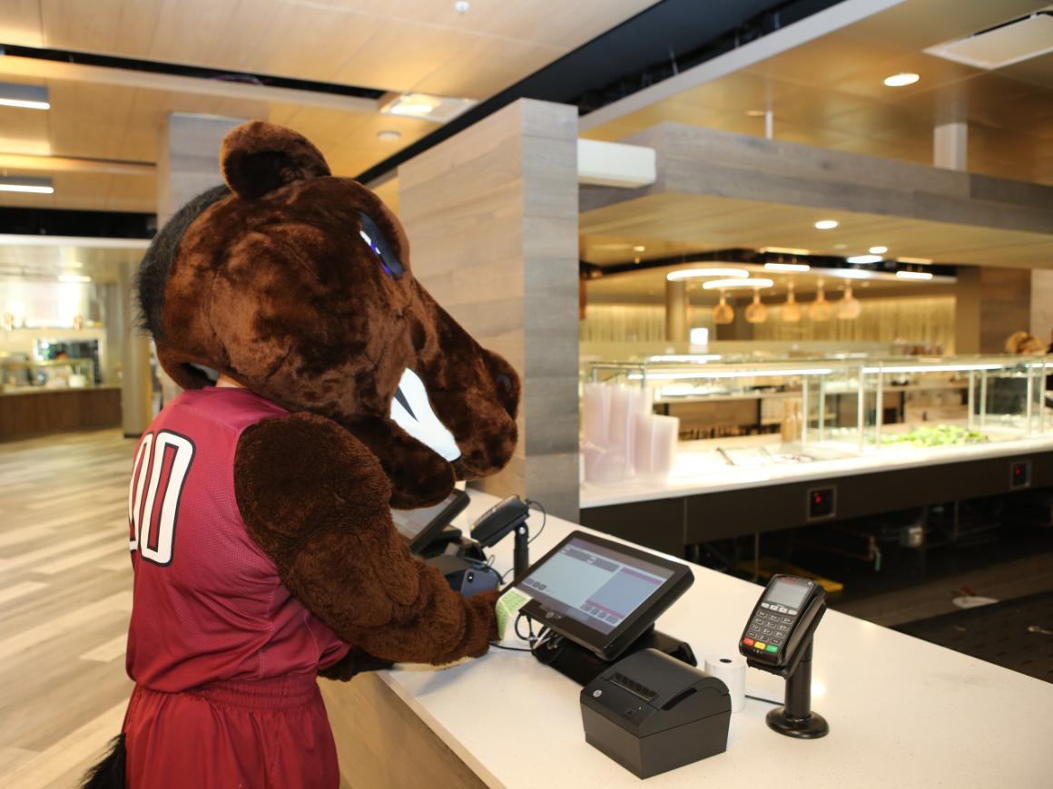 Bucky mascot in jersey at food counter.