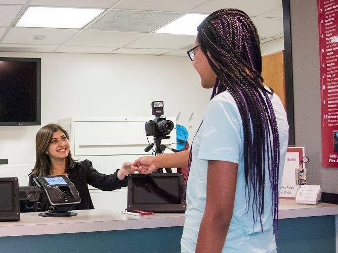 A person hands a card to another across a counter.