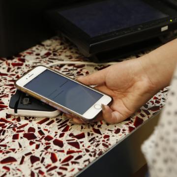 Hand holding smartphone near patterned cloth with electronics in the background.