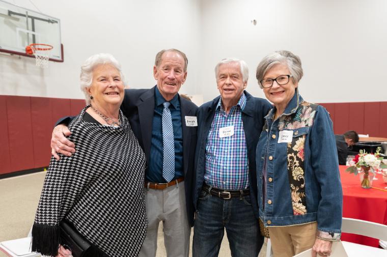 Four people stand together and smile at the camera while at a lunch honoring the Class of 1960